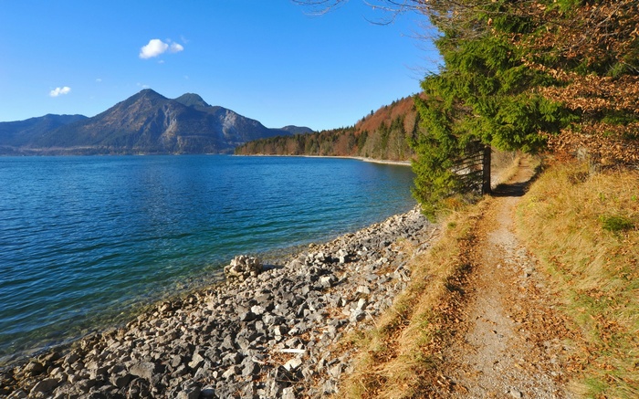 Dirt path along a rocky lake shore with mountains