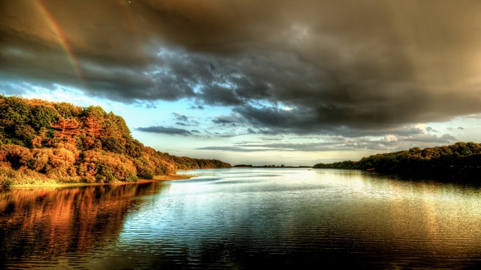 Lake with trees and stormy sky with rainbow