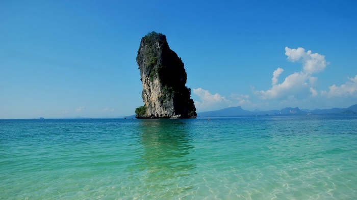 Tall rock formation in the ocean under a blue sky