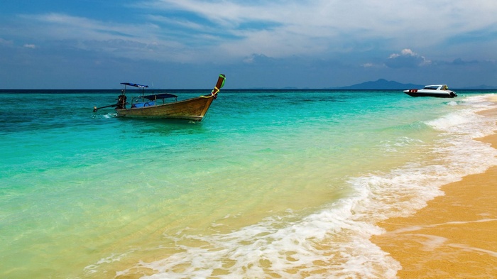 Longtail boat and speed boat in turquoise water near beach
