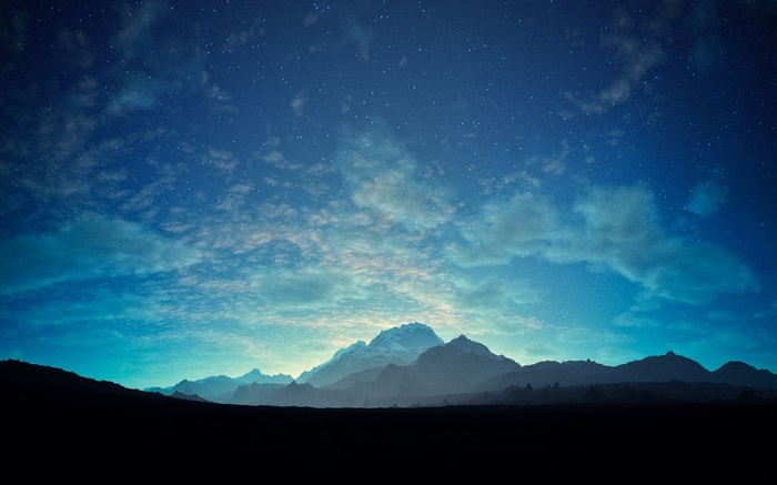 Mountains under a starry night sky with clouds
