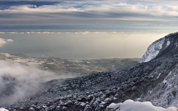 Snow-covered mountains overlooking a coastal city and the sea