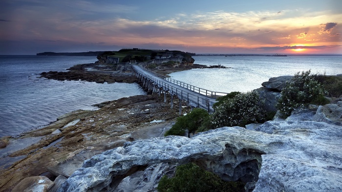 Wooden bridge connecting rocky island with fort at sunset