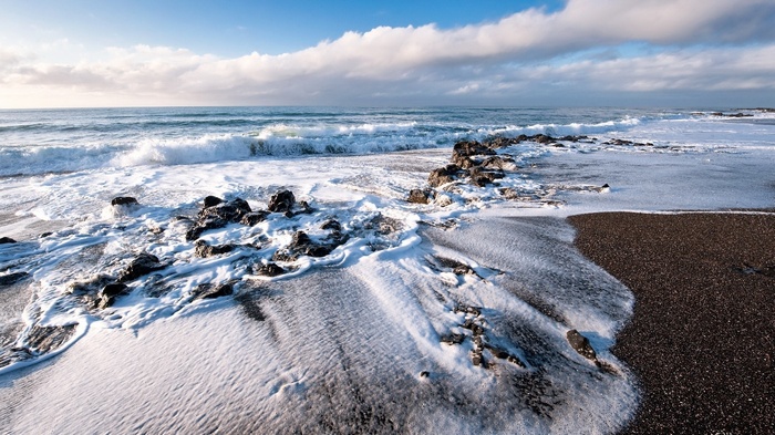 Waves crashing on a rocky, dark sand beach