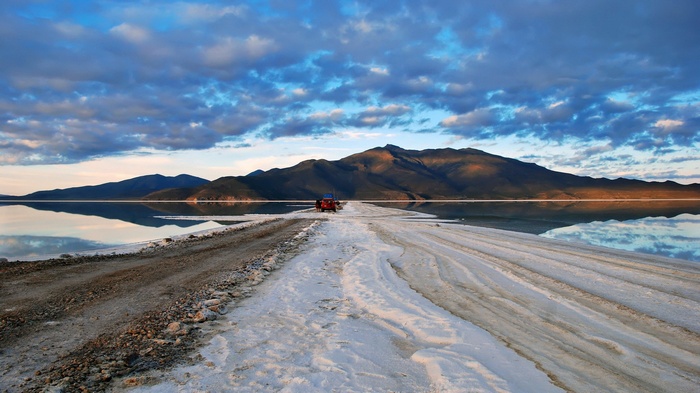 Red vehicle on a salt flat road with mountains and clouds