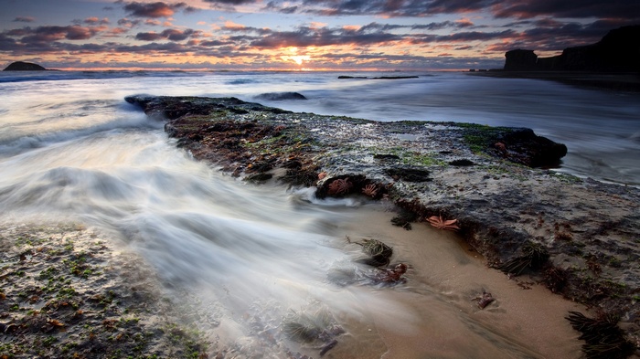 Ocean waves crashing on rocky shore at sunset