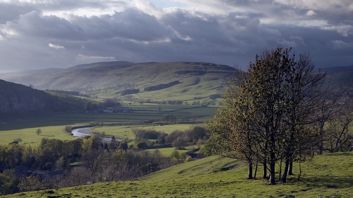 Rolling green hills and a winding river under cloudy skies