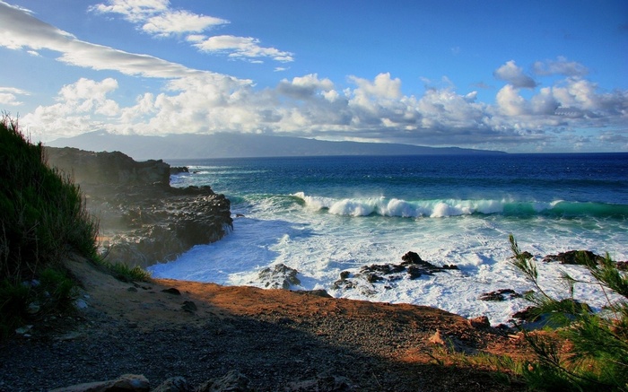 Ocean waves crash on a rocky shore with distant mountains