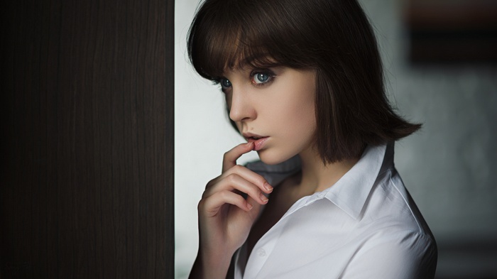 Woman with finger on lips, blue eyes, white shirt