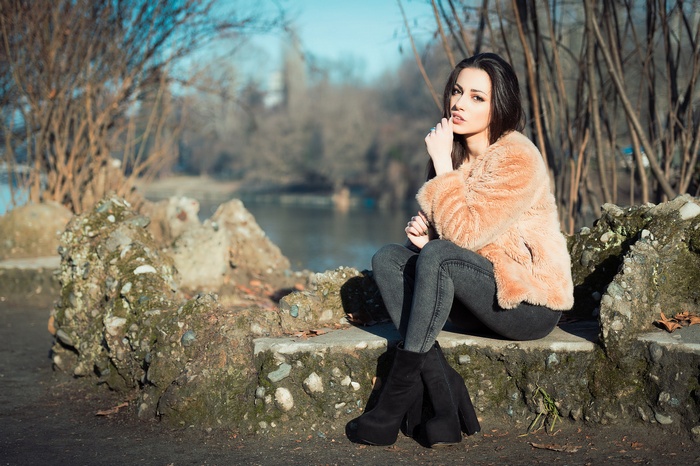 Brunette woman in fur coat sitting by lake