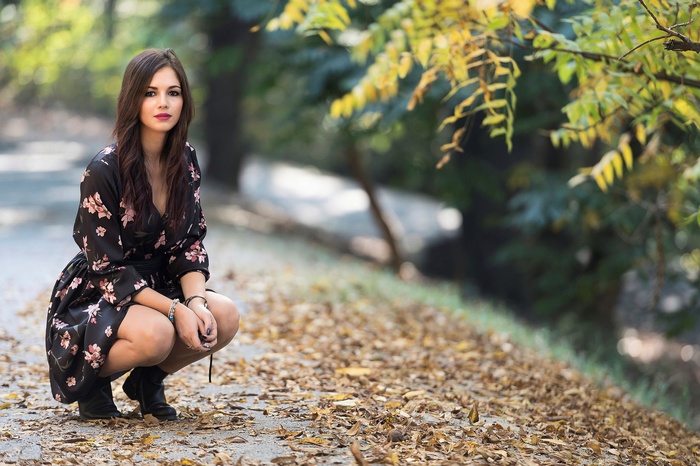 Woman in floral dress crouching in autumn park
