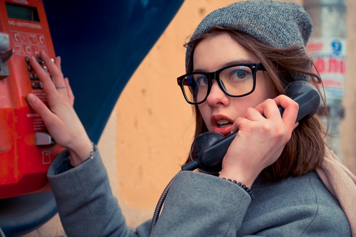 Woman with glasses using a payphone