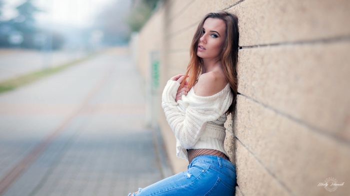 Woman in torn jeans and white sweater leaning against a wall