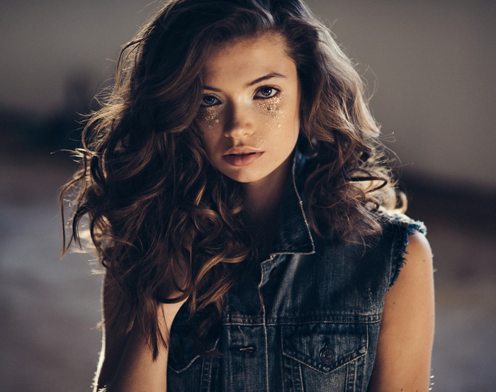 Woman with curly hair and glitter on face wearing denim vest