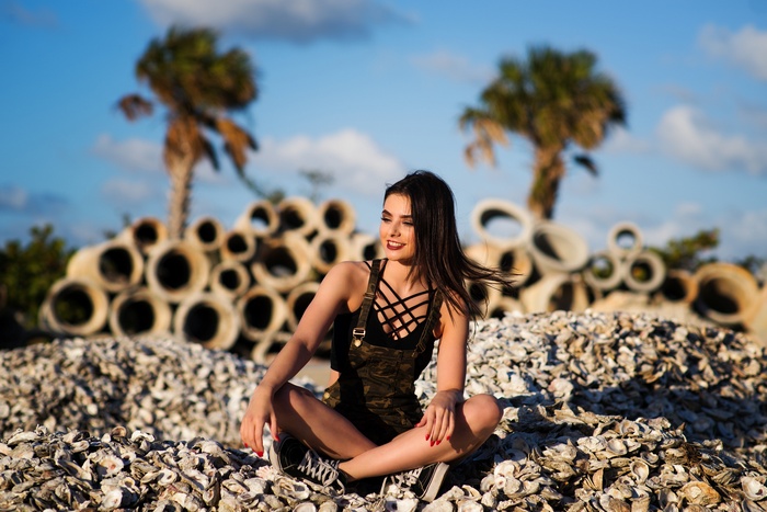 Woman in overalls sitting on shells with palm trees