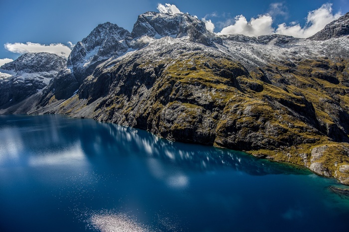 Blue lake reflecting snow-capped mountains in Fiordland National Park, New Zealand