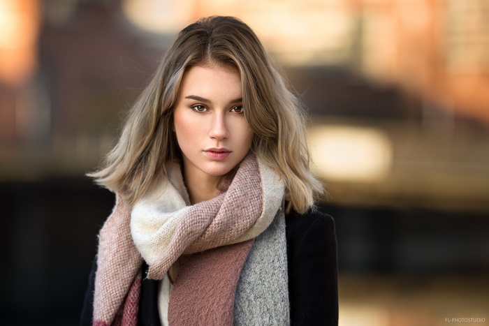 Woman with blonde hair wearing a scarf and black coat
