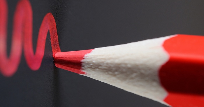 Red pencil drawing a wavy line on a dark surface