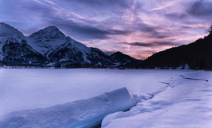 Snowy mountains and frozen lake at sunset