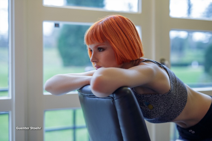 Woman with orange bob haircut leaning on chair