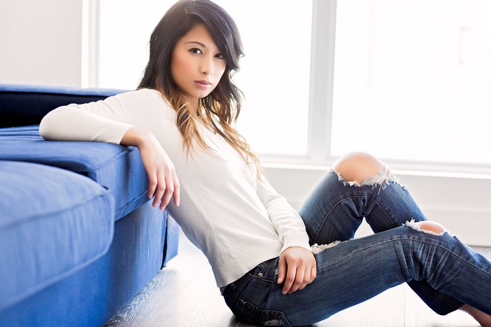 Asian woman in torn jeans sitting by a blue couch