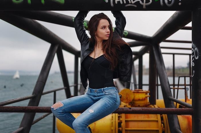 Woman in leather jacket and torn jeans sitting outdoors
