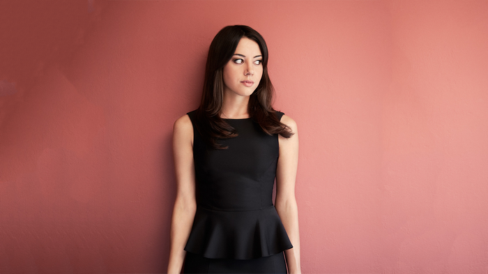 Aubrey Plaza in a black dress against a pink wall