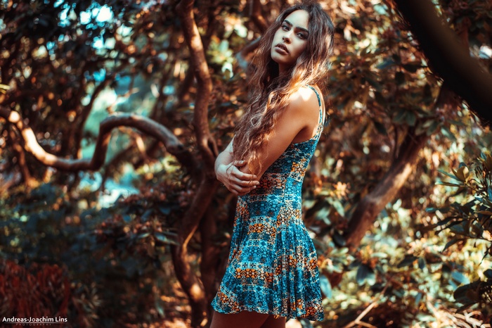 Woman in patterned dress with arms crossed in forest