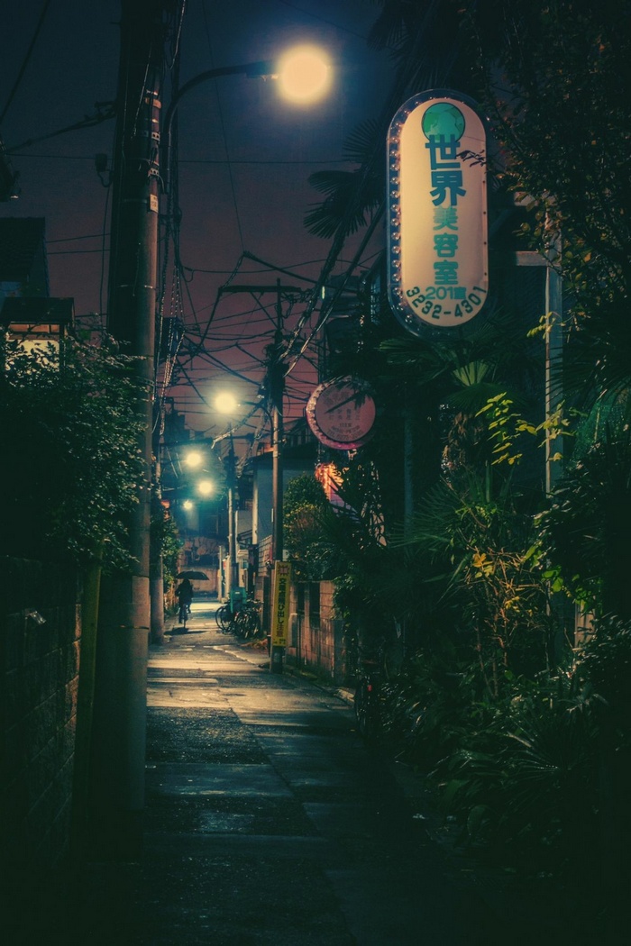 Night alley with glowing sign and person on bicycle