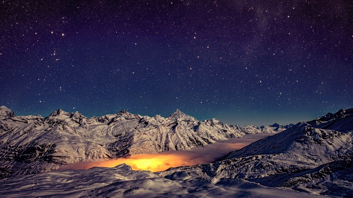 Snowy mountains under a starry night sky with glowing mist