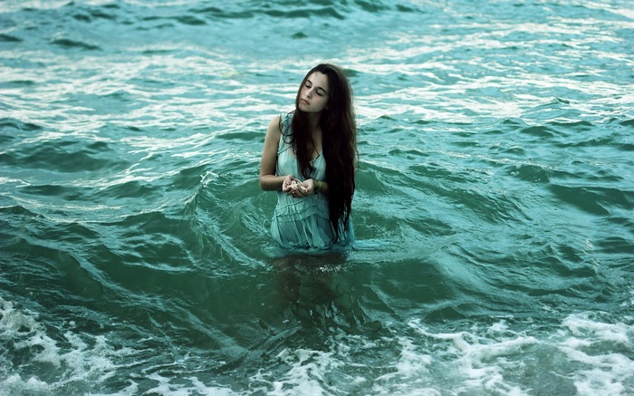 Woman in a light blue dress standing in the ocean