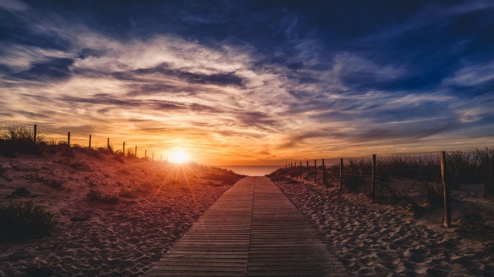 Wooden boardwalk through sand dunes towards the sea at sunset