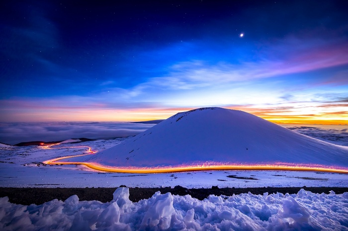 Snowy mountain road with light trails at sunset