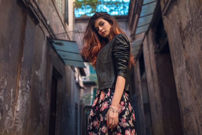 Woman in leather jacket and floral dress in alley