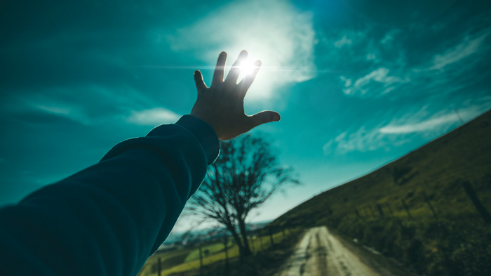 Hand reaching for the sun over a dirt road
