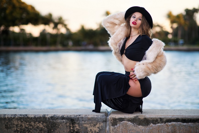 Woman in black outfit and fur coat squatting by water