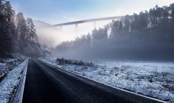 Winter road through misty forest with bridge