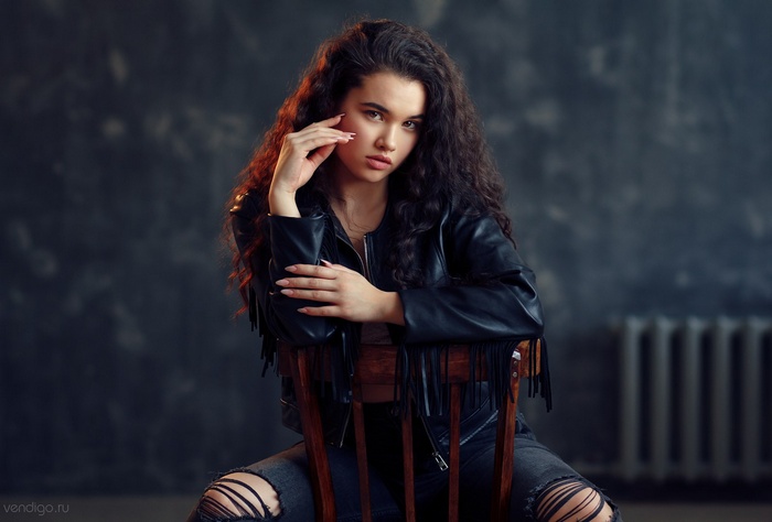 Woman in leather jacket and torn jeans sitting on a chair