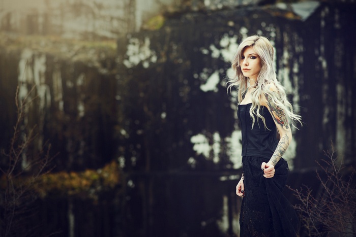 Woman with tattoos in a black dress near water