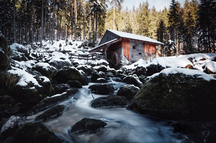 Wooden mill by a stream in a snowy forest