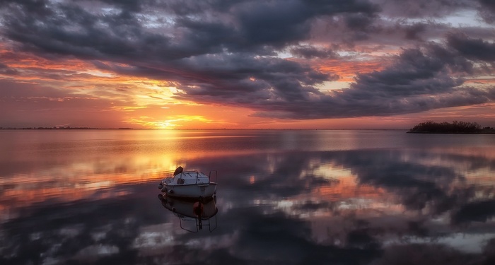 Boat on calm water at sunset with dramatic clouds
