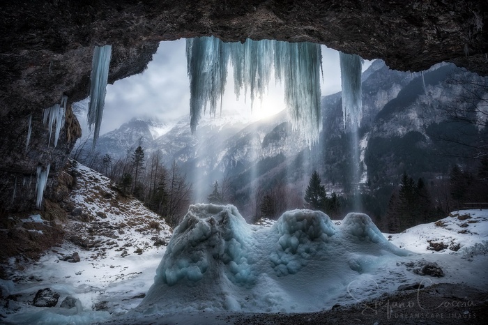 Frozen waterfall cave with icicles and snowy mountains