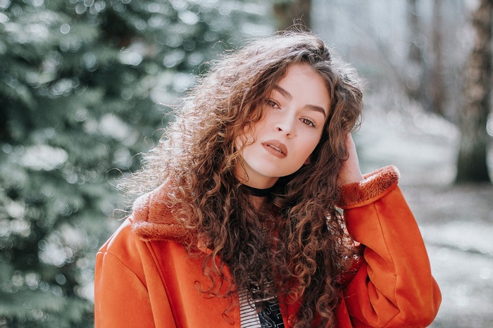 Woman with curly hair wearing an orange jacket outdoors