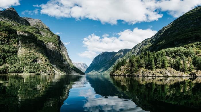 Mountains reflected in a calm fjord under a cloudy sky