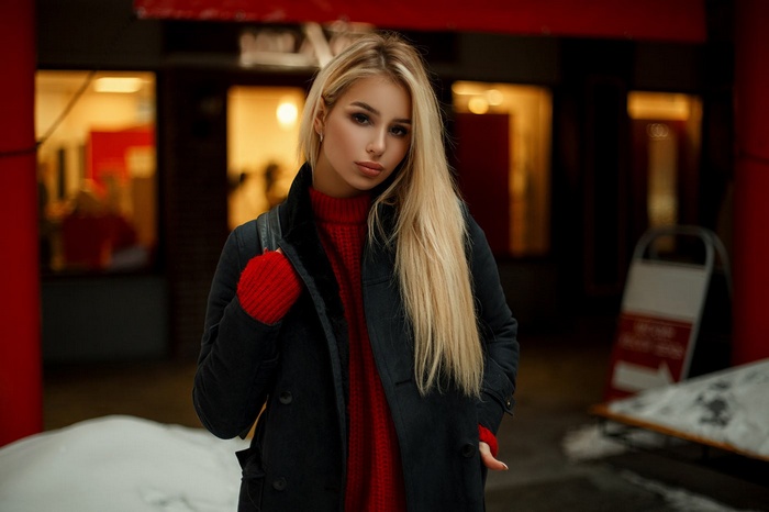 Woman with long blonde hair wearing a red sweater and black coat