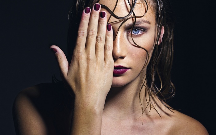 Woman with hand covering eye, wet hair, dark background