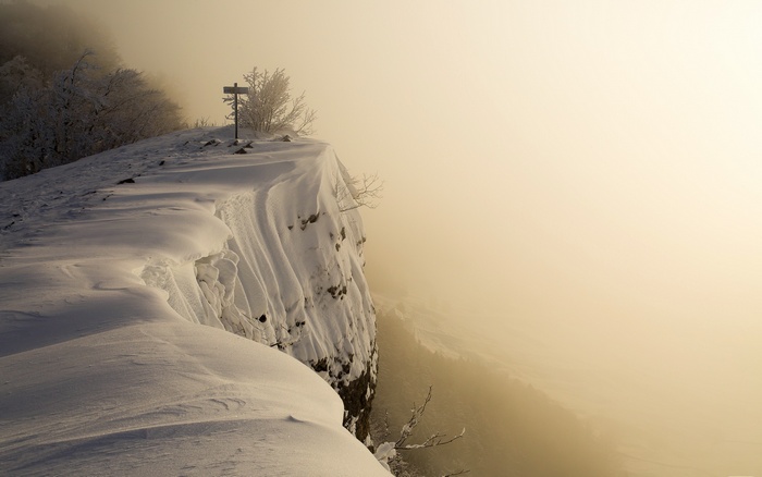 Snowy cliff edge with a signpost in winter fog