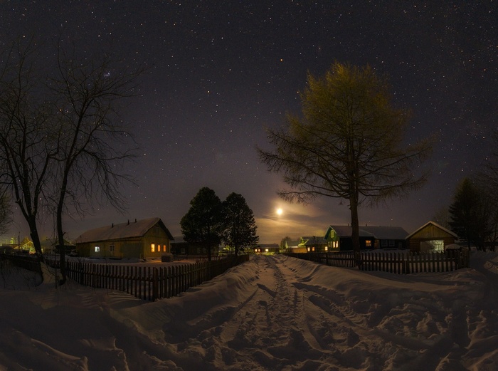 Winter village at night under starry sky with moon