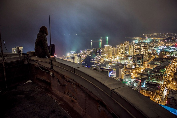 Woman sitting on a rooftop overlooking a cityscape at night