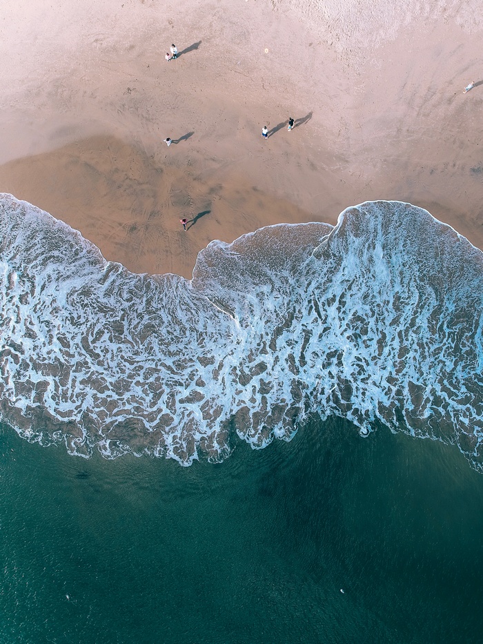 Aerial view of people walking on a sandy beach with ocean waves